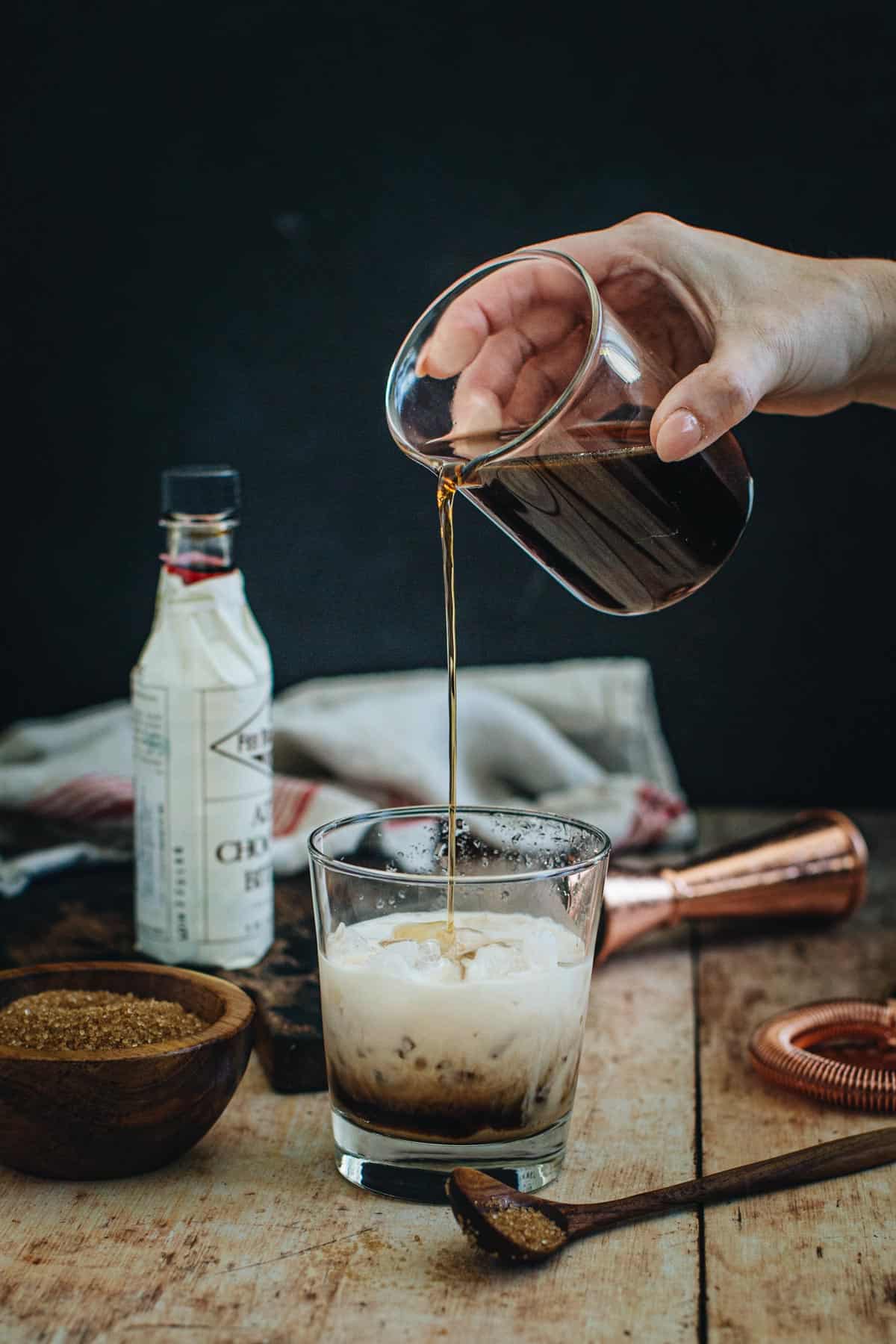 Demerara syrup pouring from a jar into a cocktail glass with ice.