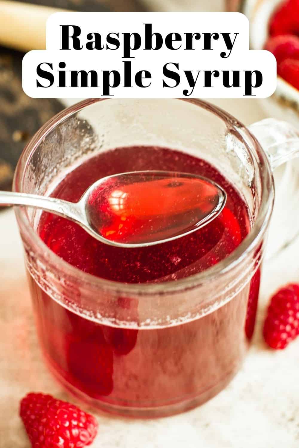 Raspberry simple syrup on a silver spoon over a glass.