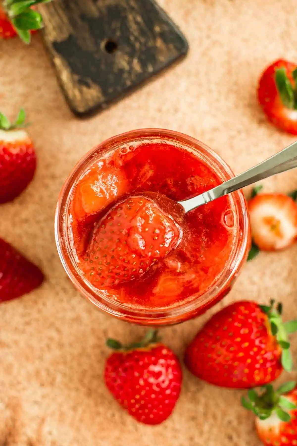 Strawberry compote in a jar with a silver serving spoon.