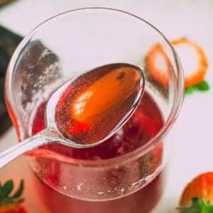 Homemade strawberry simple syrup on a spoon.