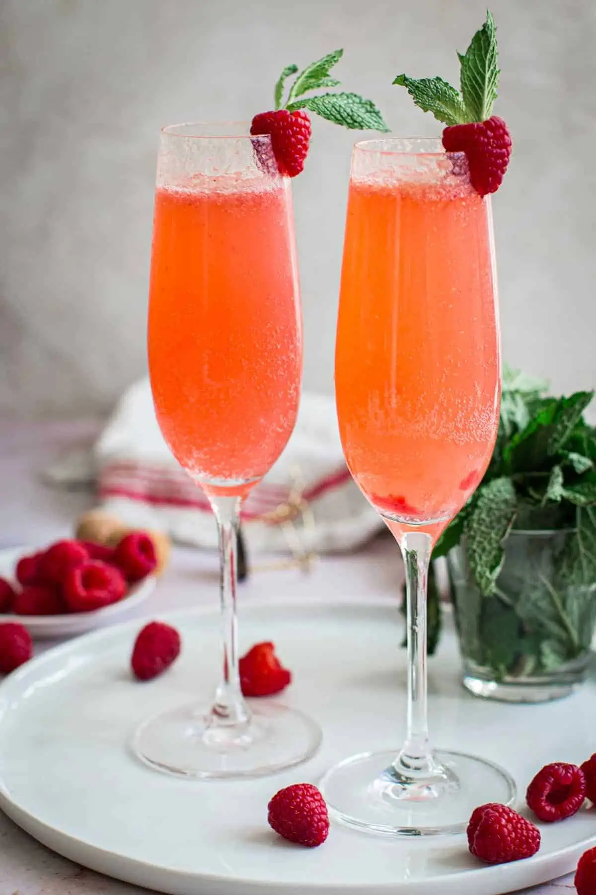 Two raspberry bellinis in flutes with fresh raspberries and mint for garnish.