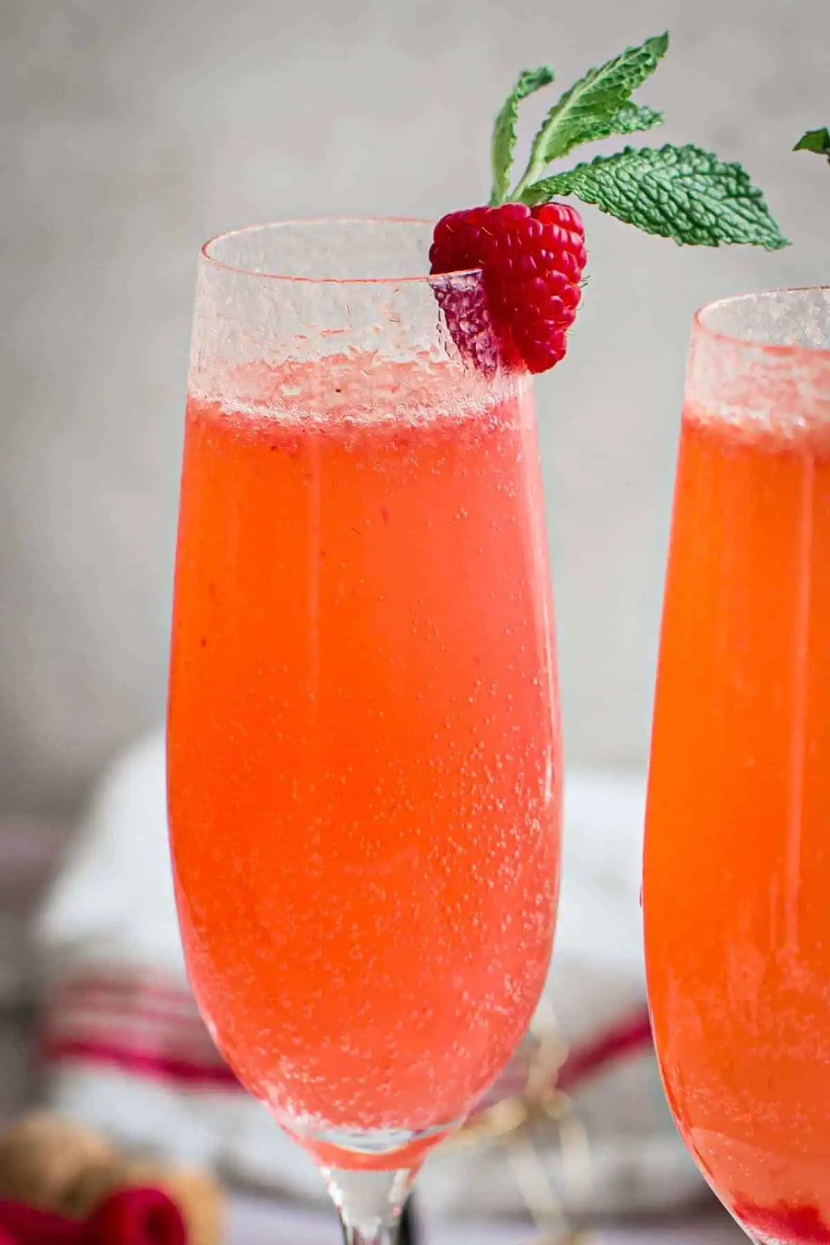 A raspberry bellini topped with a fresh raspberry and mint leaf for garnish.