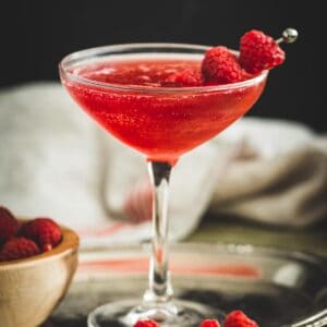 Raspberry martini with fresh raspberries on a cocktail skewer.