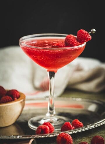 Raspberry martini with fresh raspberries on a cocktail skewer.