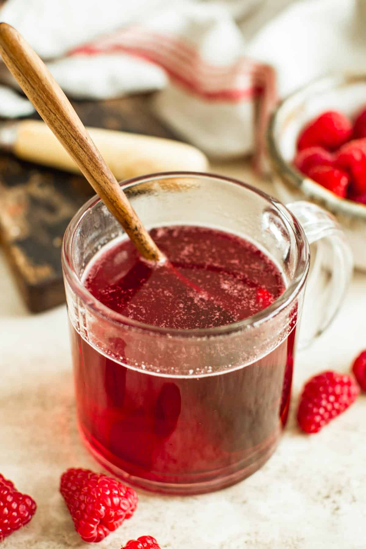 Raspberry simple syrup in a glass with a wooden spoon.