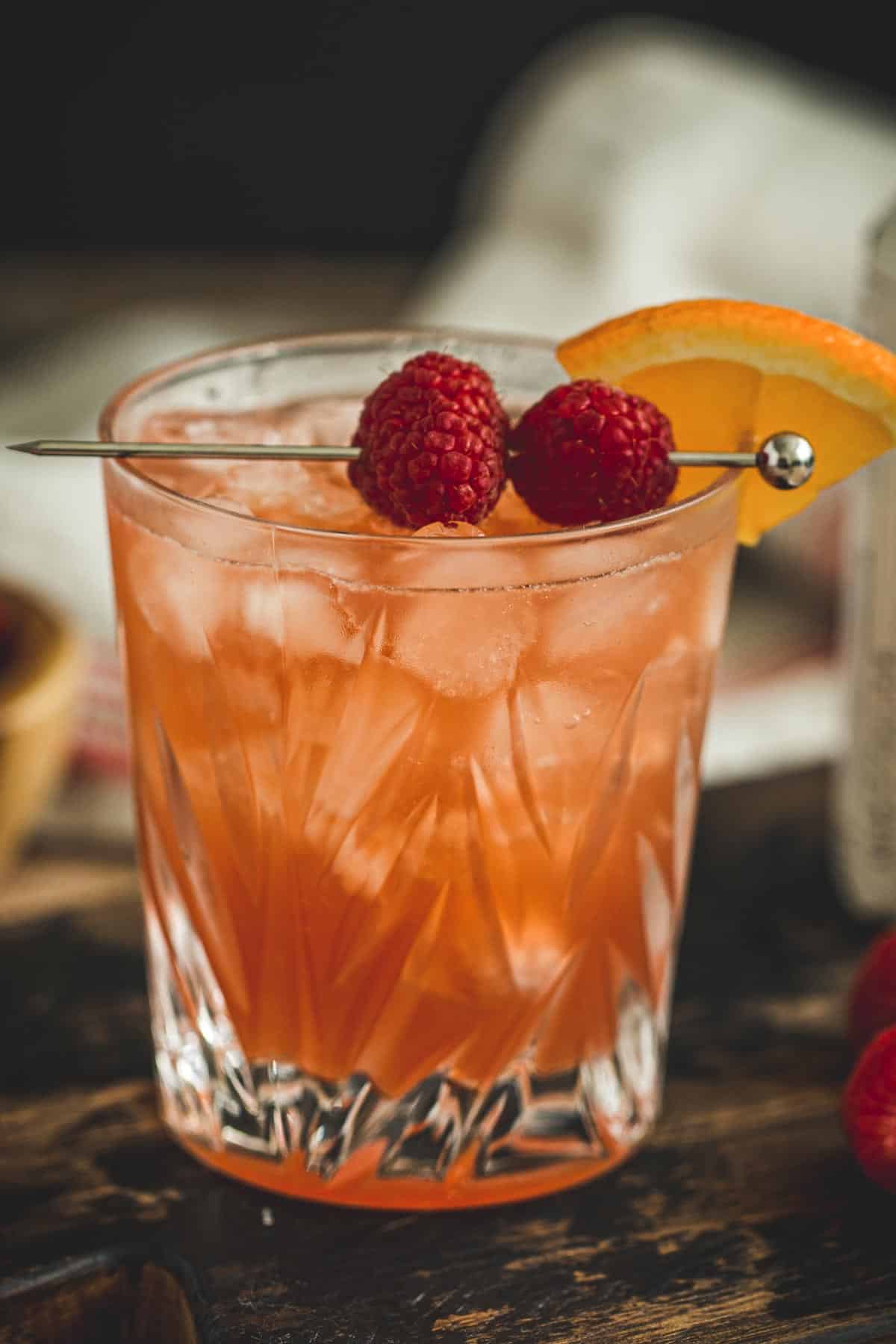 Raspberry sour cocktail with fresh raspberries and an orange wedge for garnish.