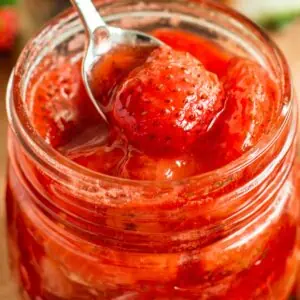 Strawberry compote in a jar with a silver serving spoon.