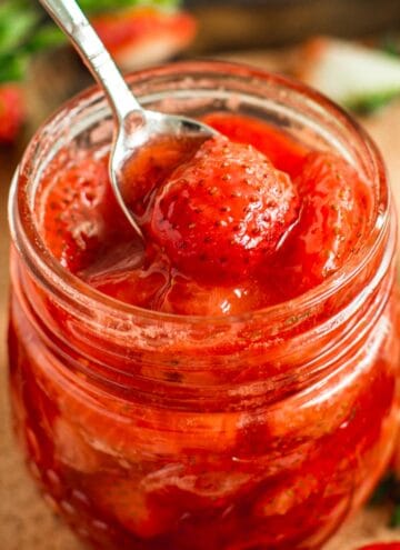 Strawberry compote in a jar with a silver serving spoon.