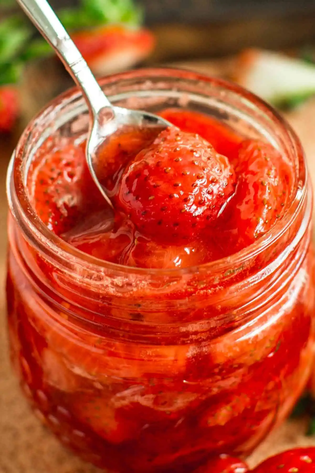 Strawberry compote in a jar with a spoon inserted.