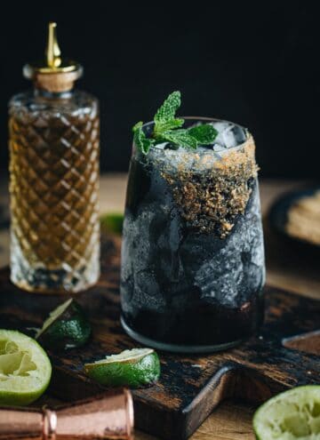 Black margarita with a brown sugar rim and mint leaf garnish.