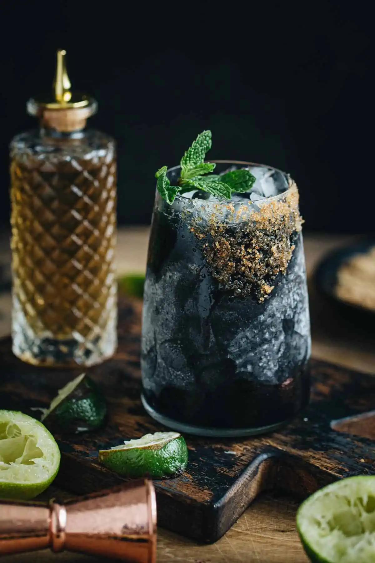 Black margarita with a brown sugar rim and mint leaf garnish.