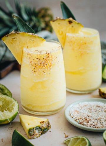 Two frozen pineapple margaritas with salted rims and pineapple wedges for garnish.