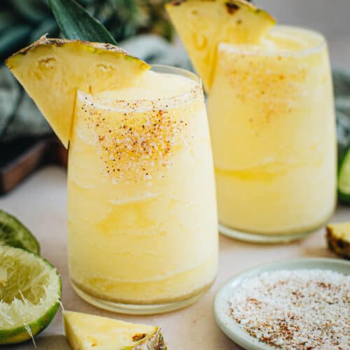 Two frozen pineapple margaritas with salted rims and pineapple wedges for garnish.