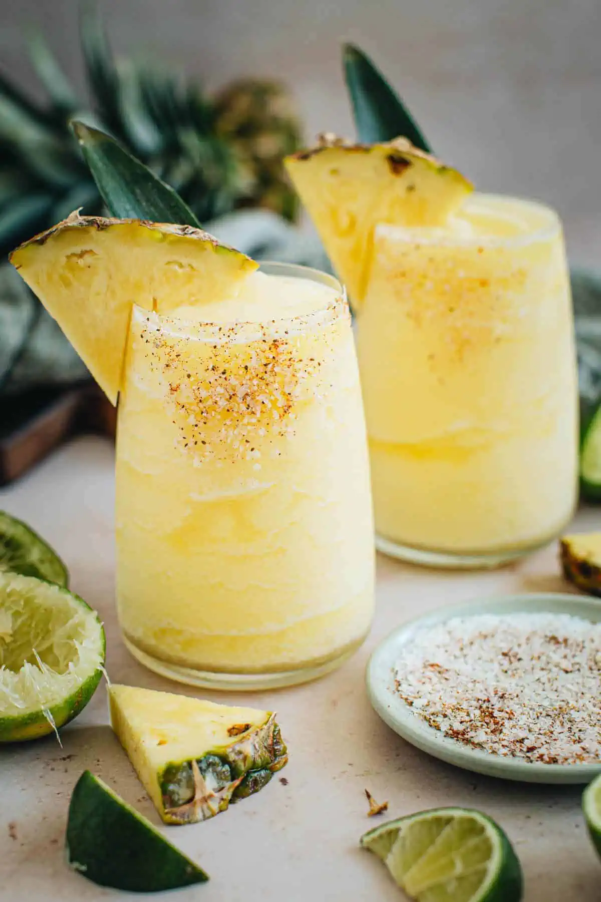 Two frozen pineapple margaritas with salted rims and pineapple wedges for garnish.