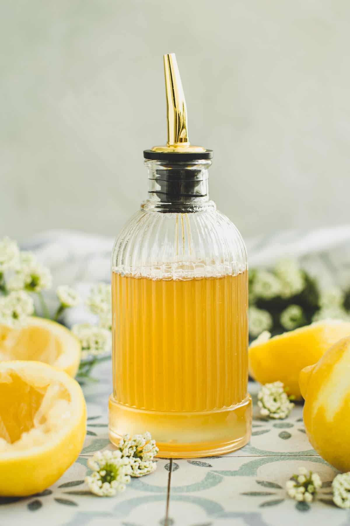 Lemon syrup in a bottle with lemons surrounding it.