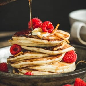 Maple syrup pancakes topped with raspberries and more maple syrup.