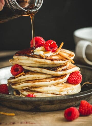 Maple syrup pancakes topped with raspberries and more maple syrup.