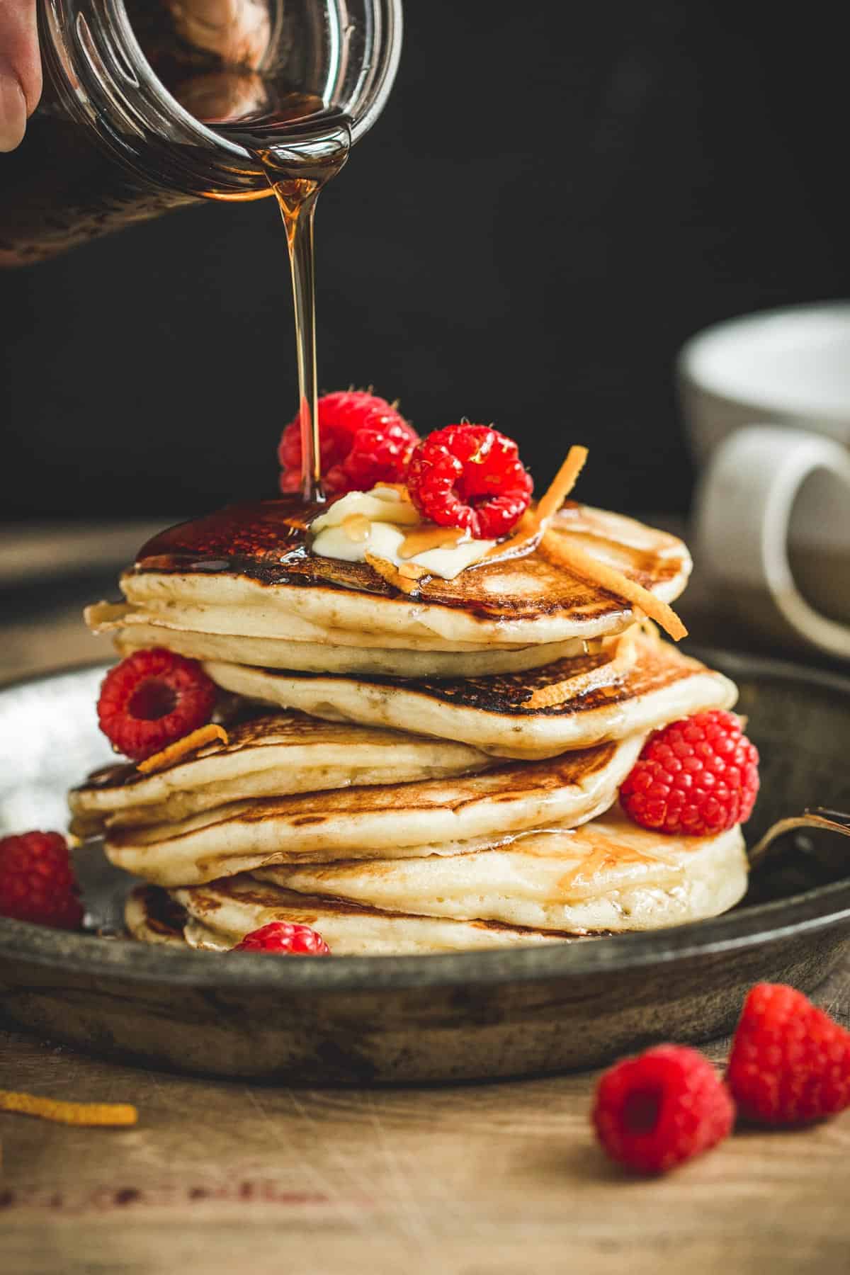 Maple syrup pancakes topped with raspberries and more maple syrup.