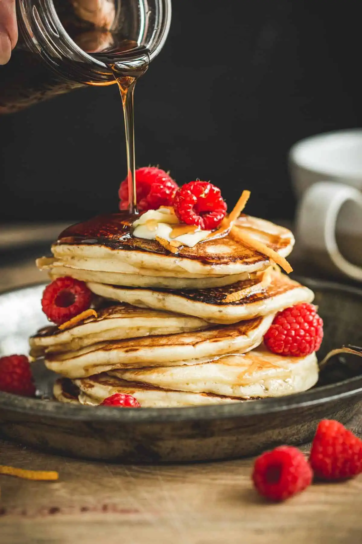 Maple syrup pancakes topped with raspberries and more maple syrup.