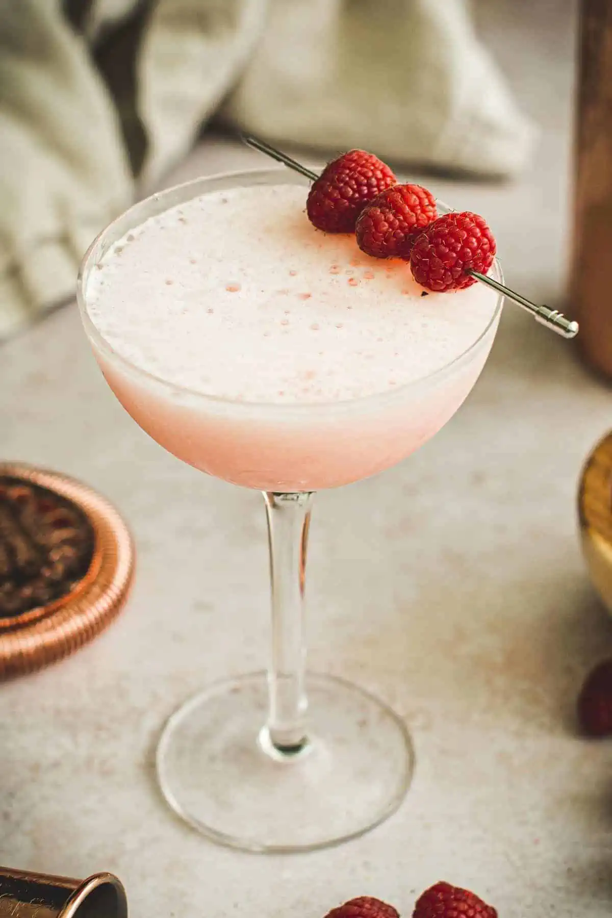 Raspberry cocktail in a coupe glass with fresh raspberries for garnish.