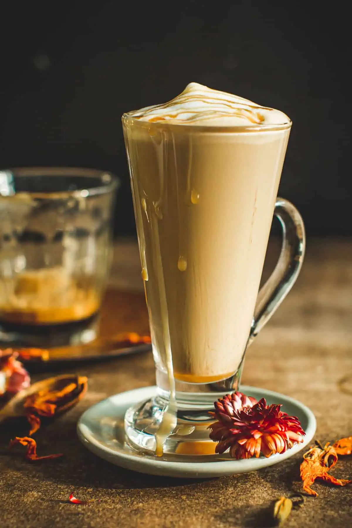 Caramel latte in a glass topped with foam and caramel drizzle.