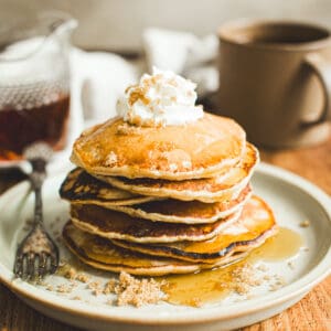 Stack of brown sugar pancakes topped with whipped cream and syrup.