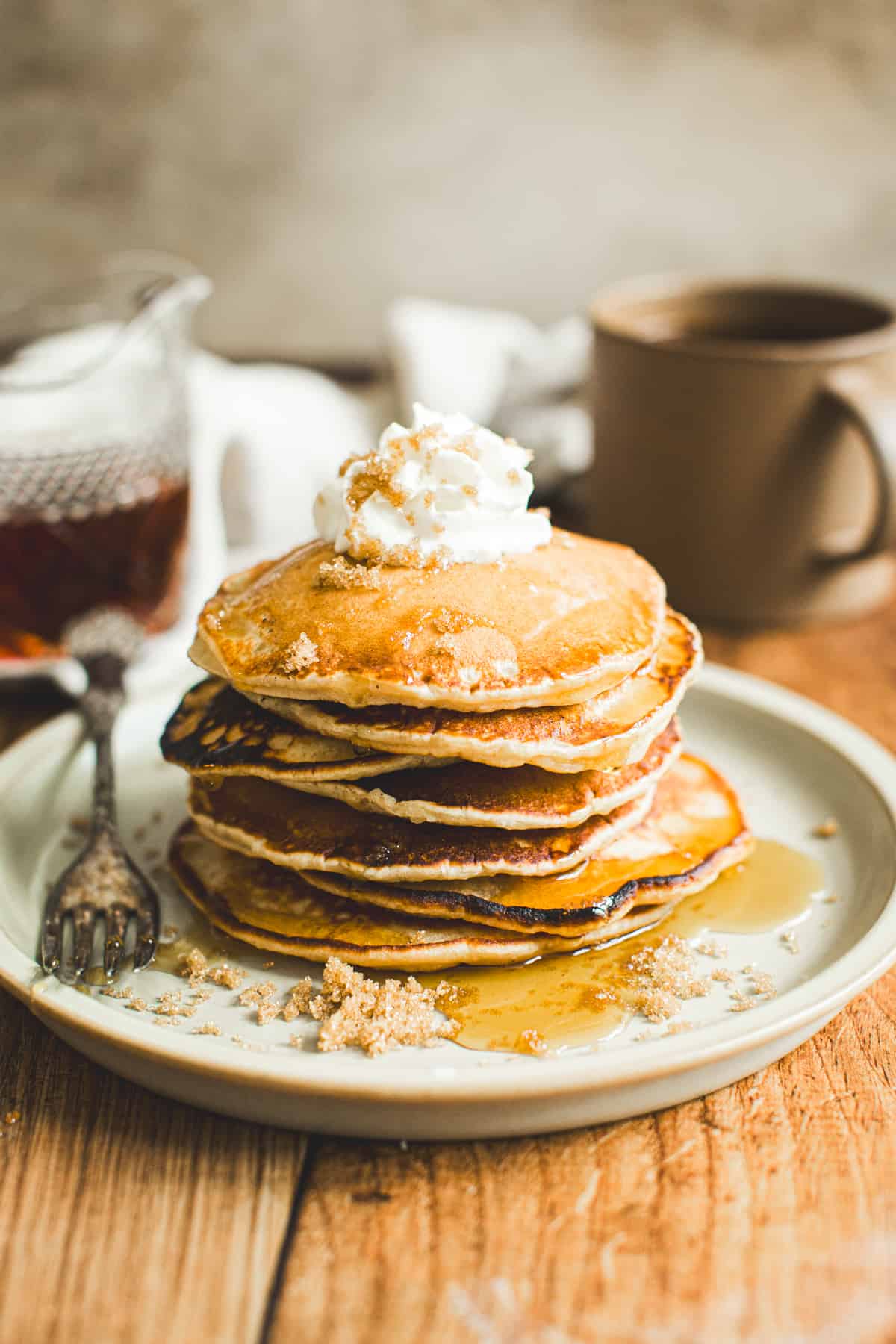 Stack of brown sugar pancakes topped with whipped cream and syrup.