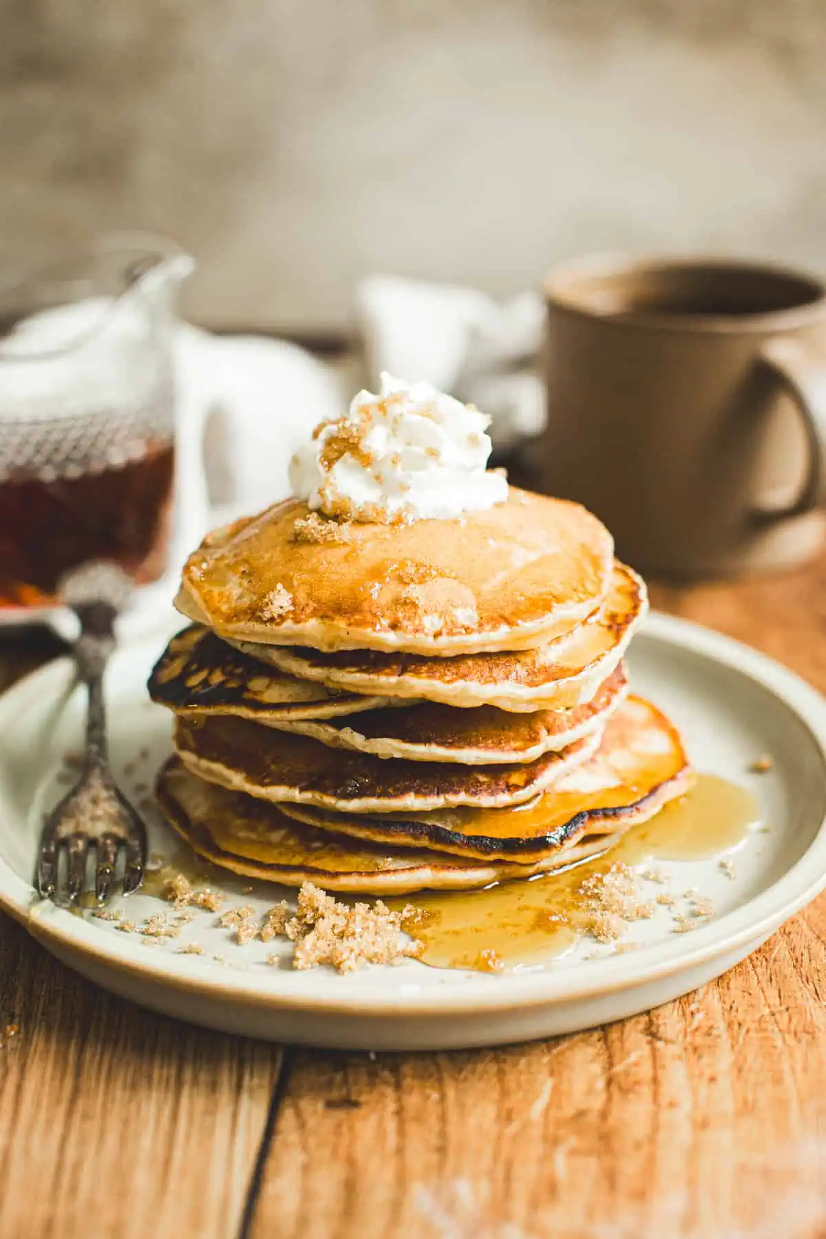 Stack of brown sugar pancakes topped with whipped cream and syrup.