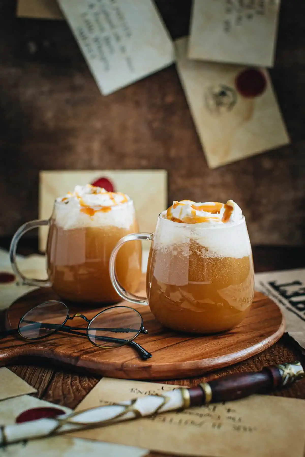 Hot butterbeer in glass mugs topped with whipped cream.