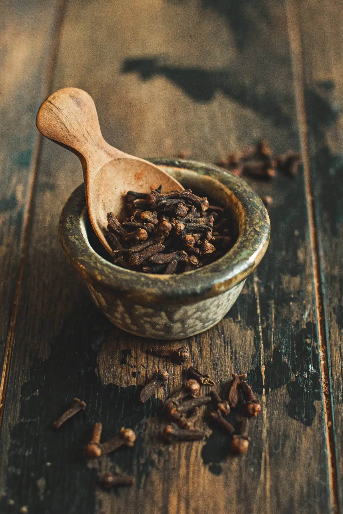 Cloves in a bowl with a wooden spoon.
