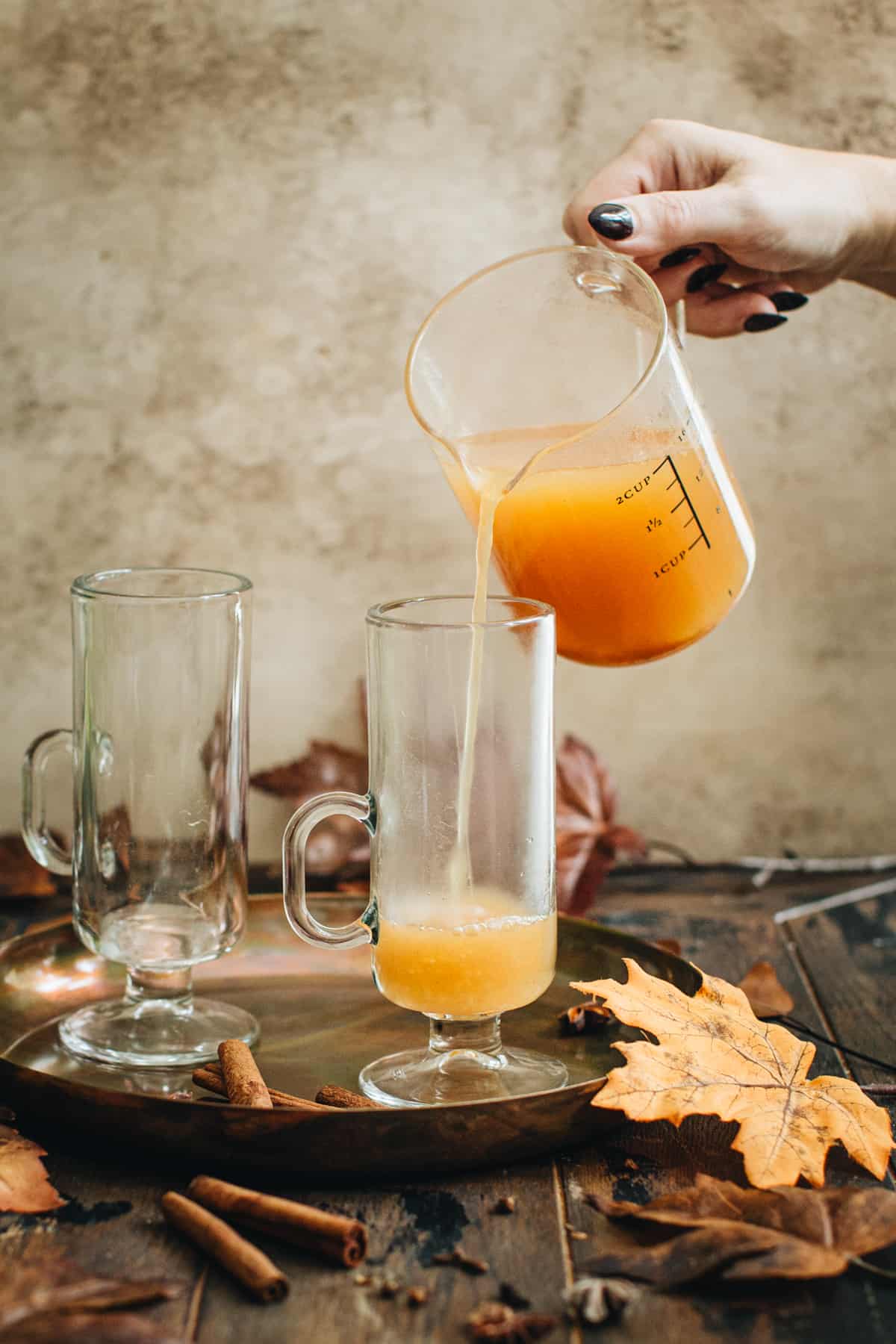 Pouring hot apple cider into a tall glass mug for an Apple Cider Hot Toddy.