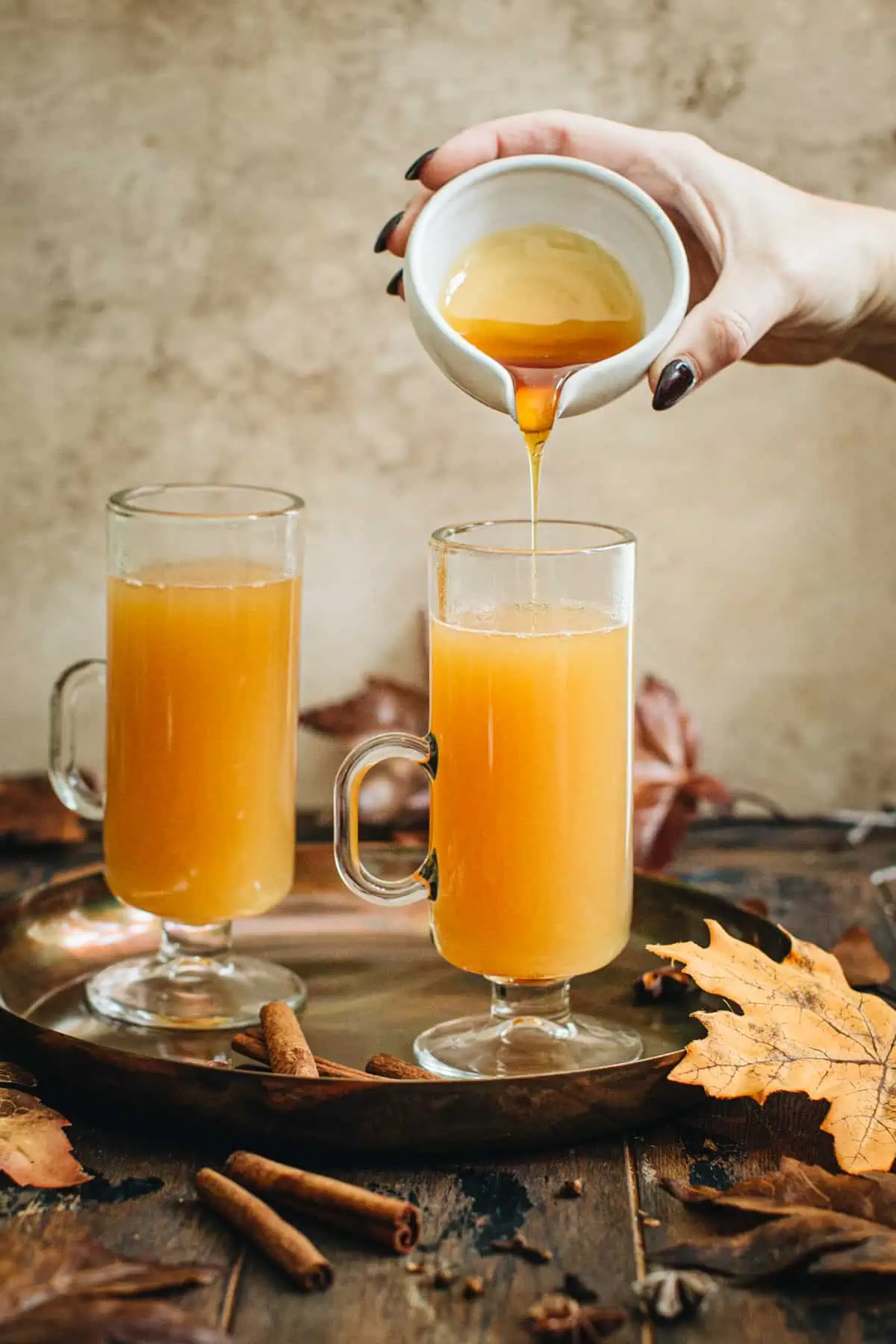 Dripping honey over hot apple cider for an Apple Cider Hot Toddy.