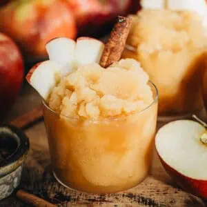 Apple cider slushie with sliced apples and a cinnamon stick for garnish.