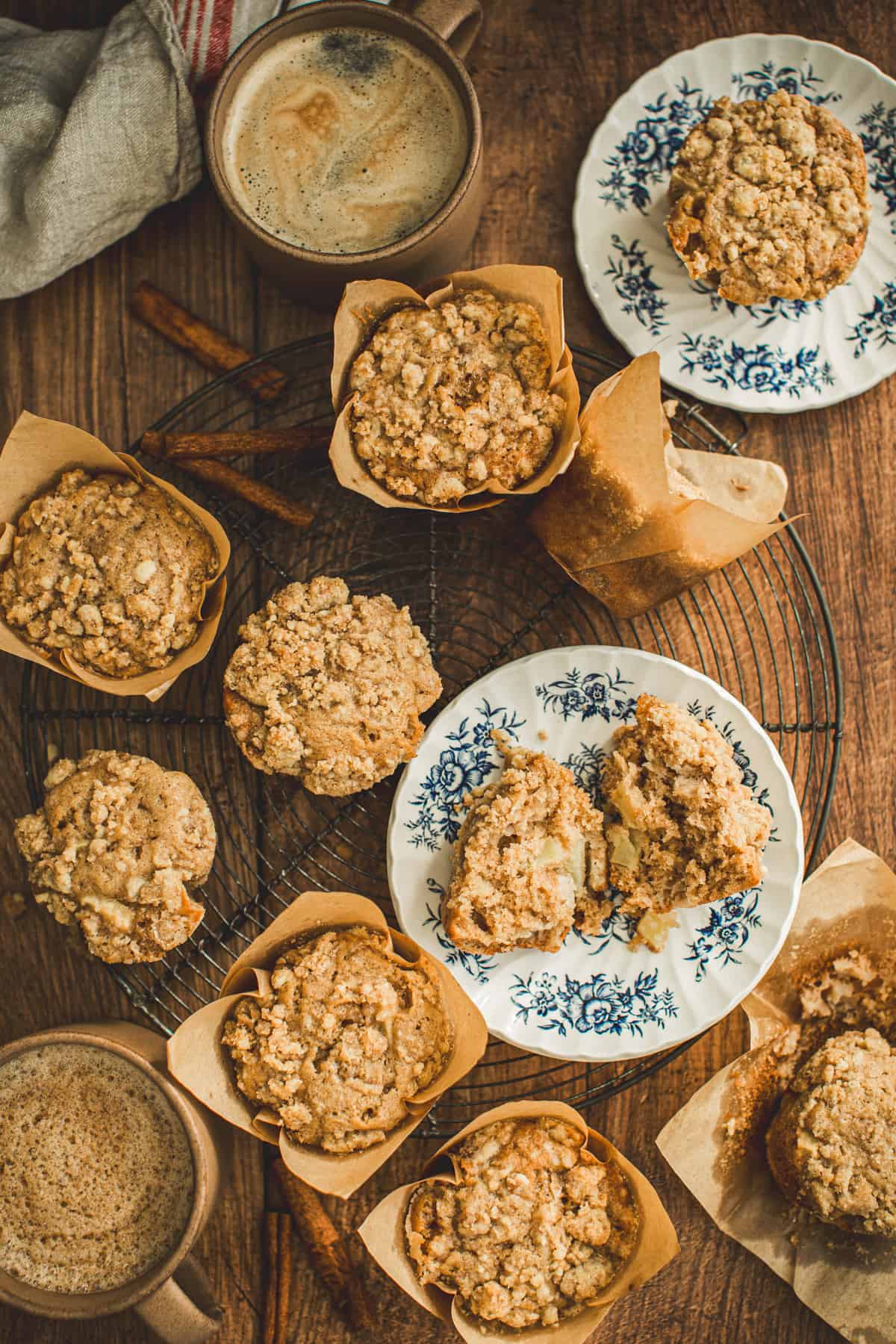 Apple cinnamon muffins with crumble topping on a round wire rack and on blue and white plates.