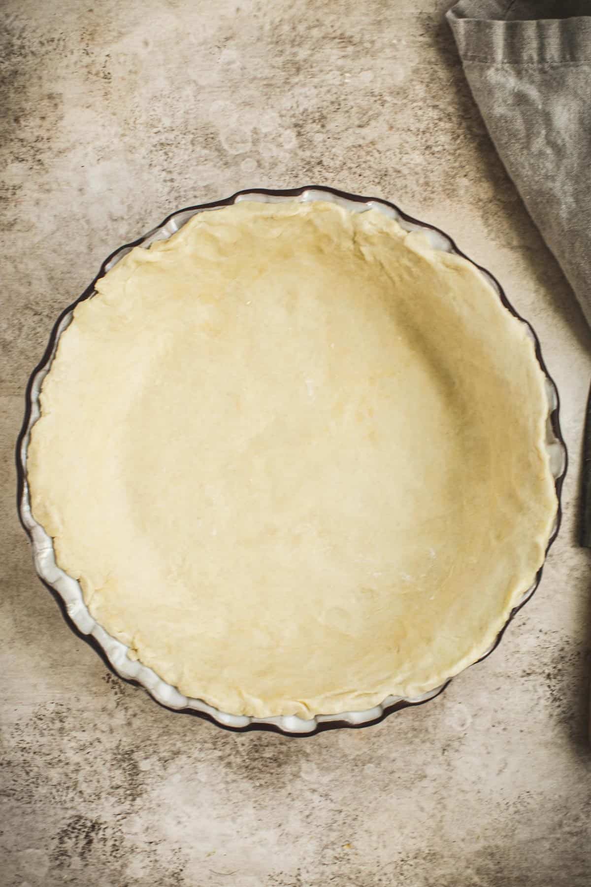 Flaky pie crust in a pie dish for apple cranberry pie.