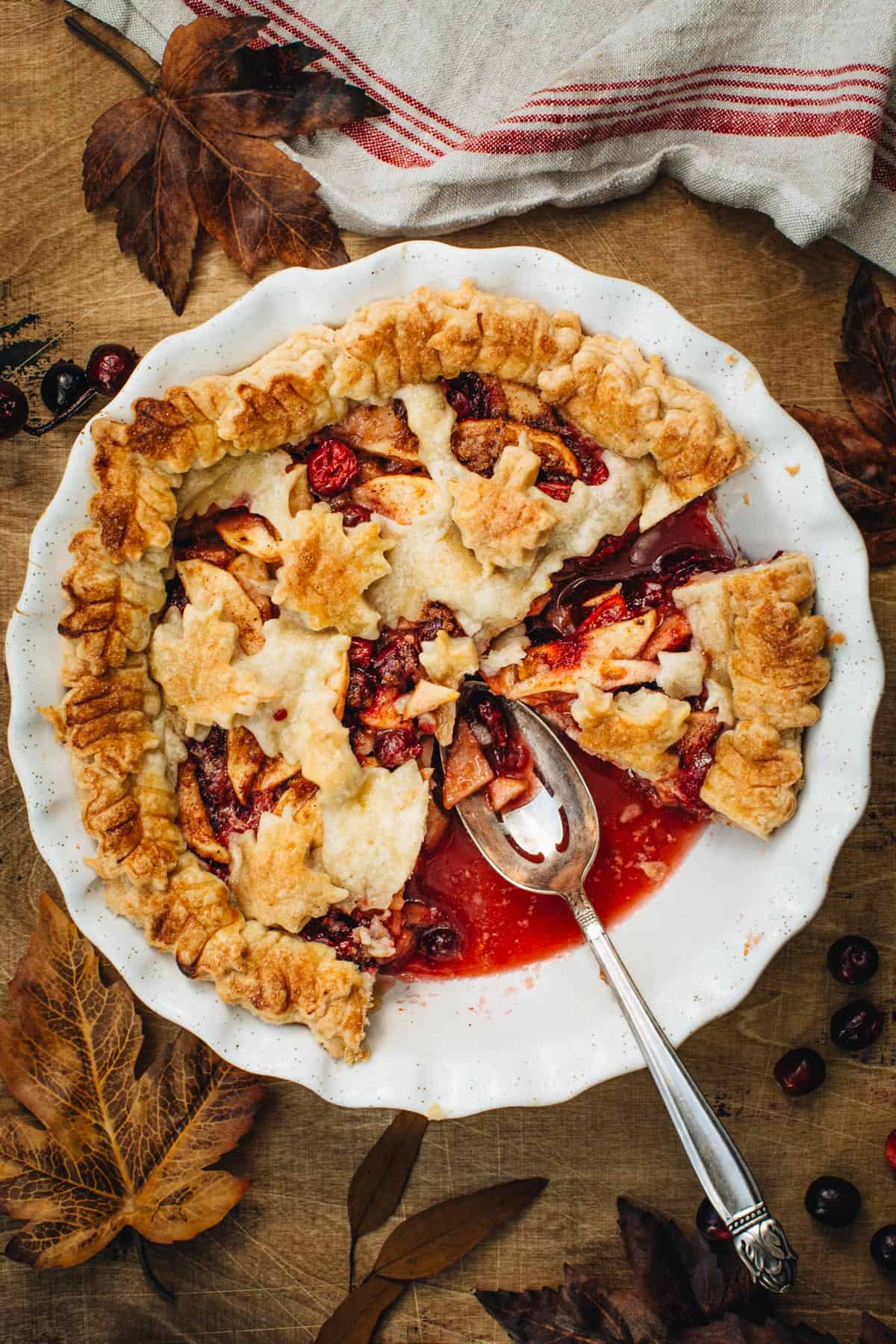 Apple cranberry pie sliced with a spoon sitting in the pie dish where a slice is missing.