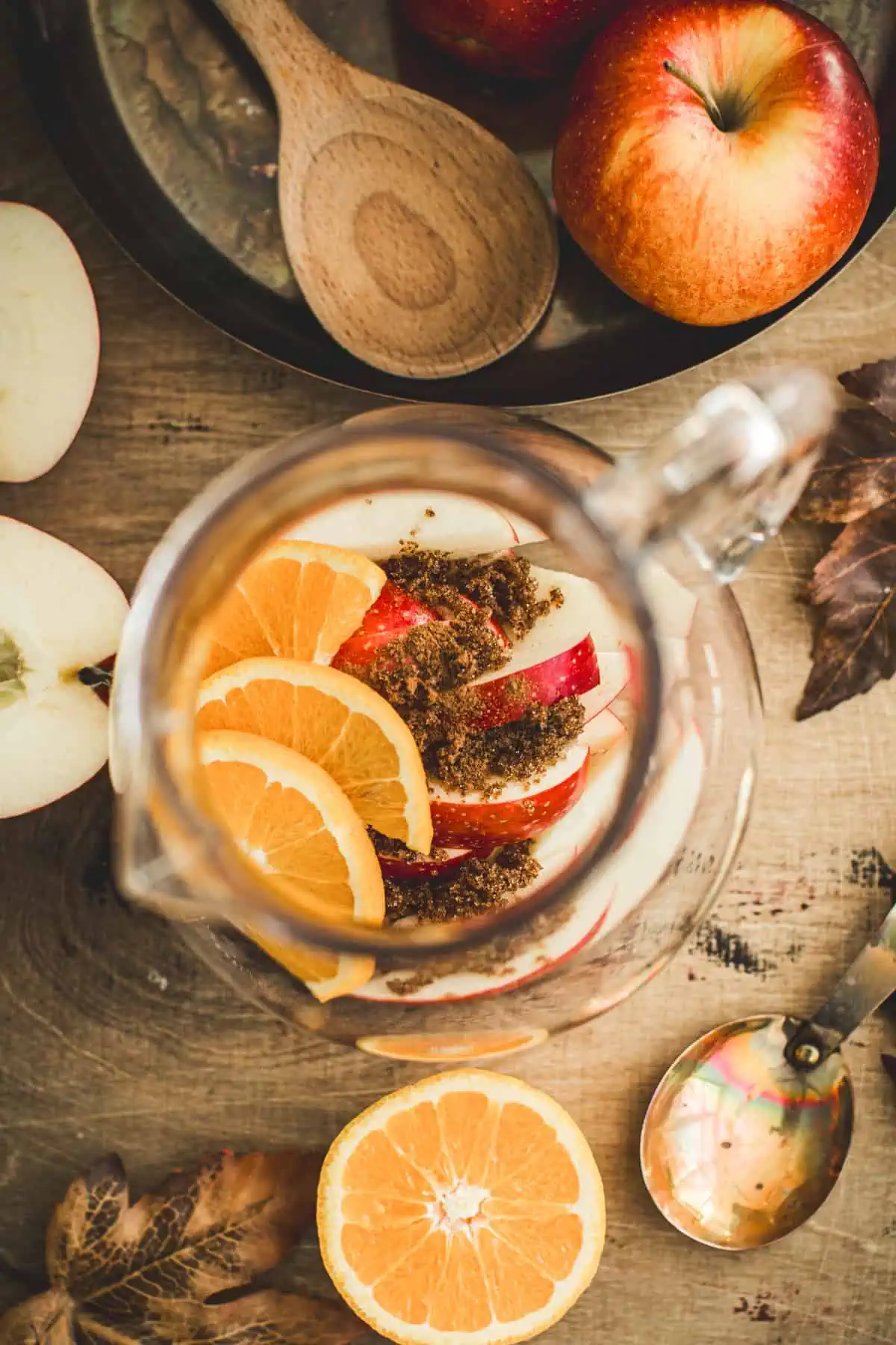 Fruits, sugar, and spices in a pitcher for making apple sangria.