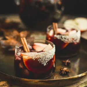 Apple sangria in a glass with a sugared rim and cinnamon stick for garnish.