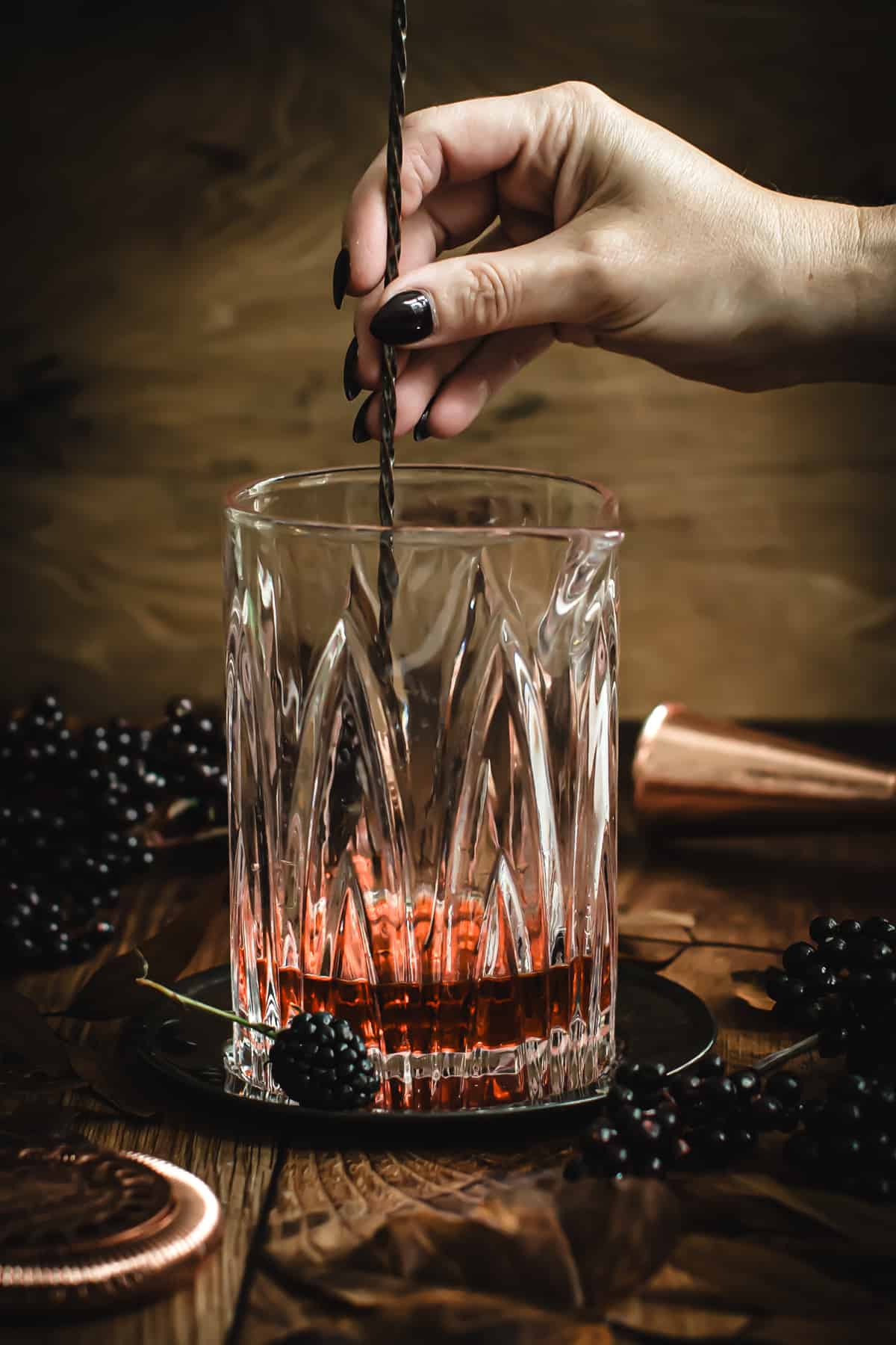 Stirring the ingredients for a Black Manhattan in a cocktail mixing glass using a cocktail spoon.