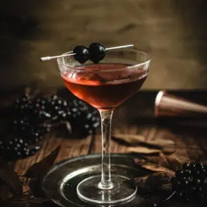 Black Manhattan in a martini glass garnished with cherries on a cocktail pick.