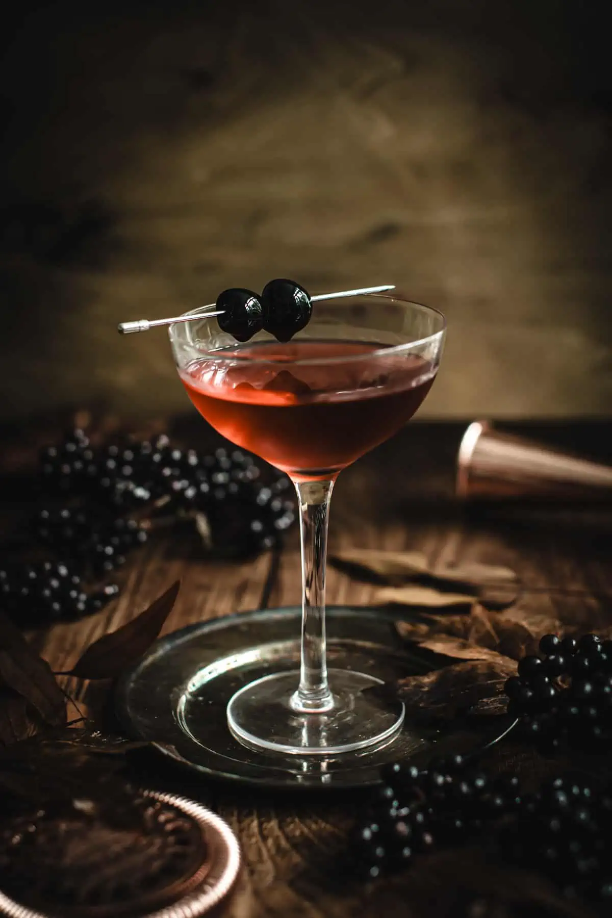 Black Manhattan in a martini glass garnished with cherries on a cocktail pick.