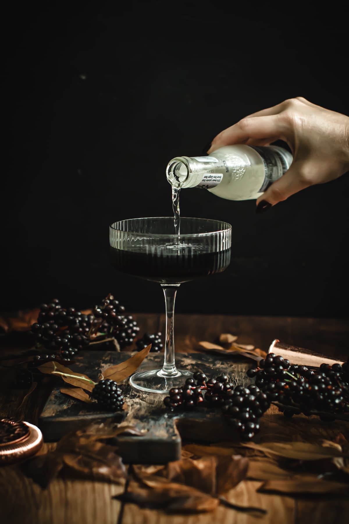 Pouring ginger beer over a black martini.