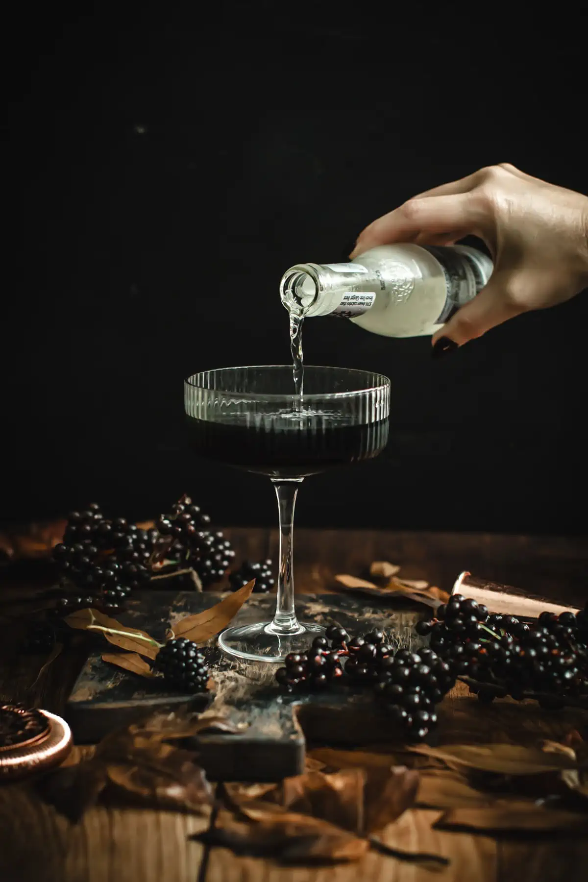 Pouring ginger beer over a black martini.