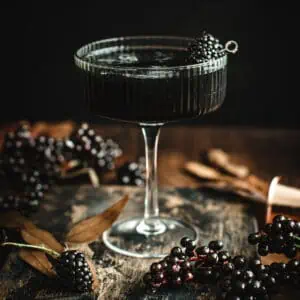 Black martini with a blackberry garnish in a ribbed martini glass.