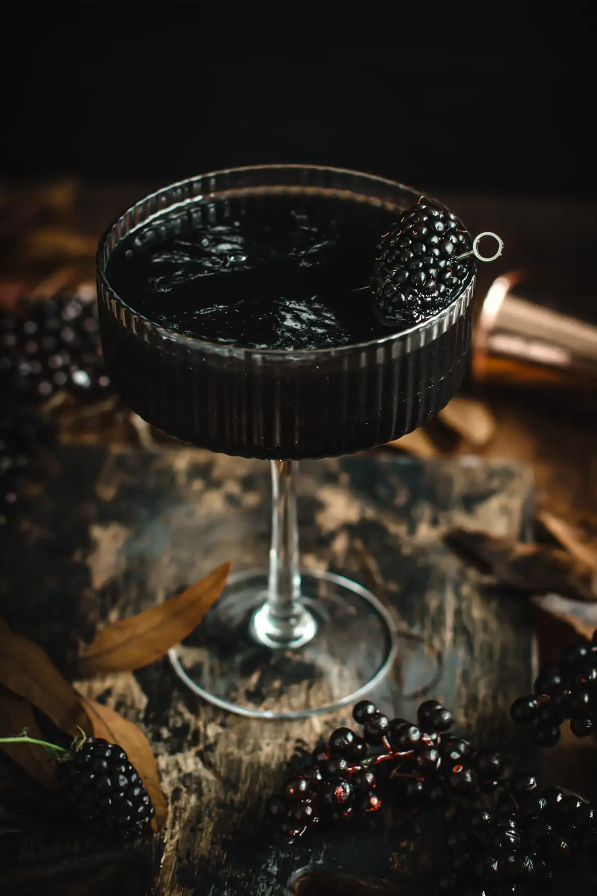A black martini in a martini glass with a blackberry for garnish.