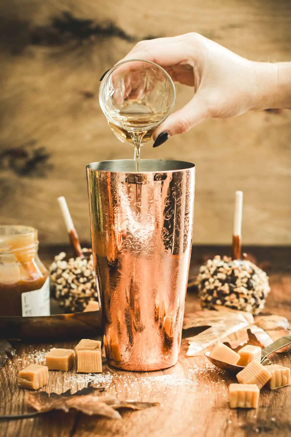 Pouring caramel apple martini ingredients into a cocktail shaker.