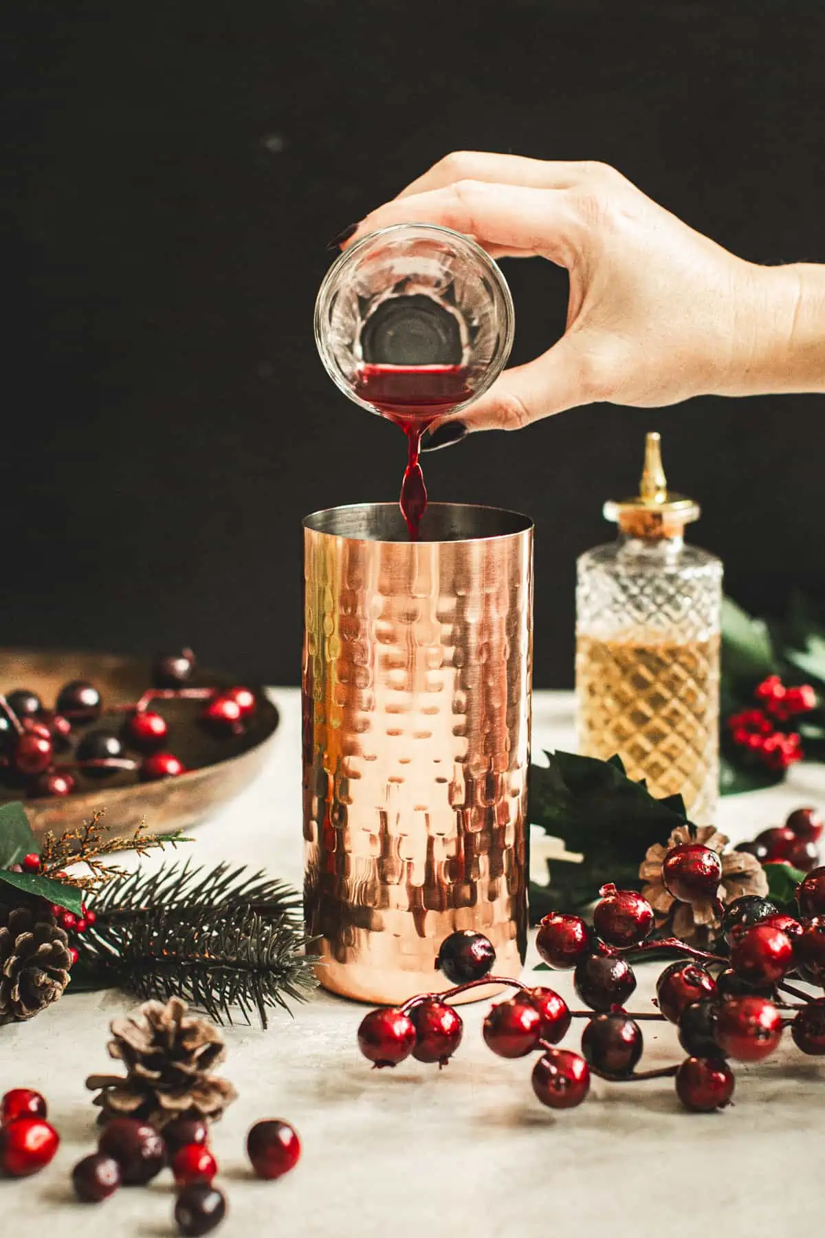 Pouring cranberry juice into a cocktail shaker for a Cranberry Martini.