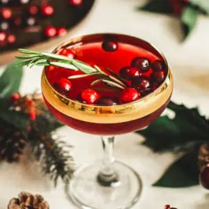 Cranberry martini in a cocktail glass with a rosemary sprig and fresh cranberries for garnish.