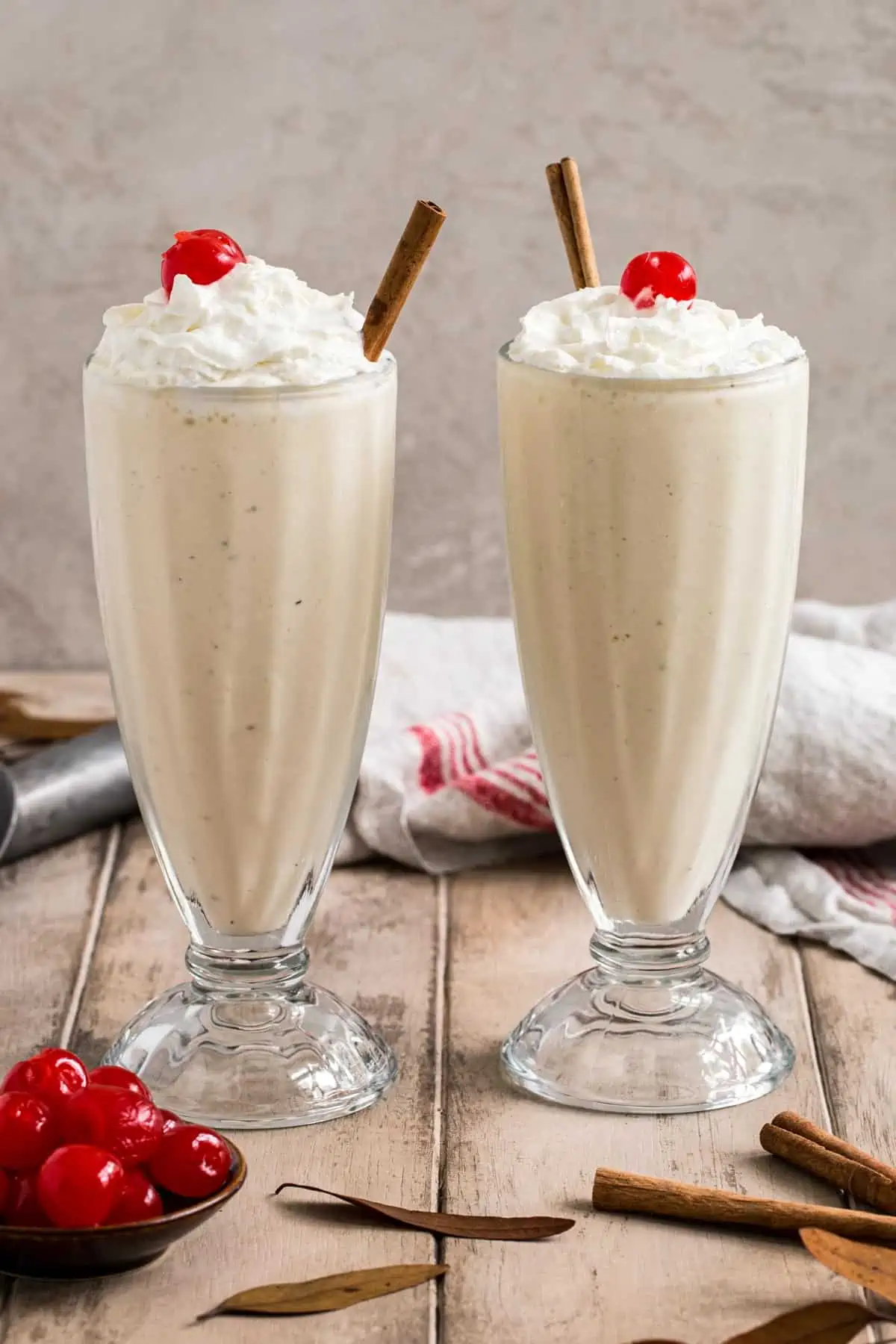 Eggnog milkshakes topped with whipped cream, cherries, and a cinnamon stick in milkshake glasses.