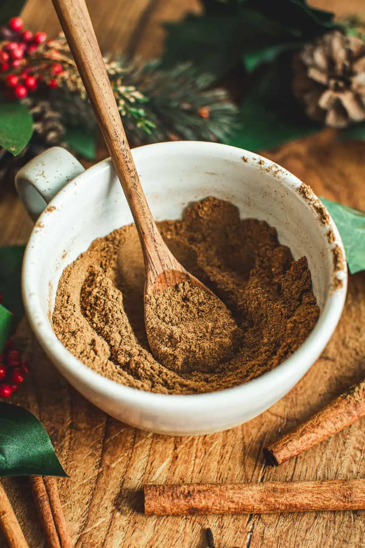 Gingerbread spice mix in a coffee mug with a wooden spoon.